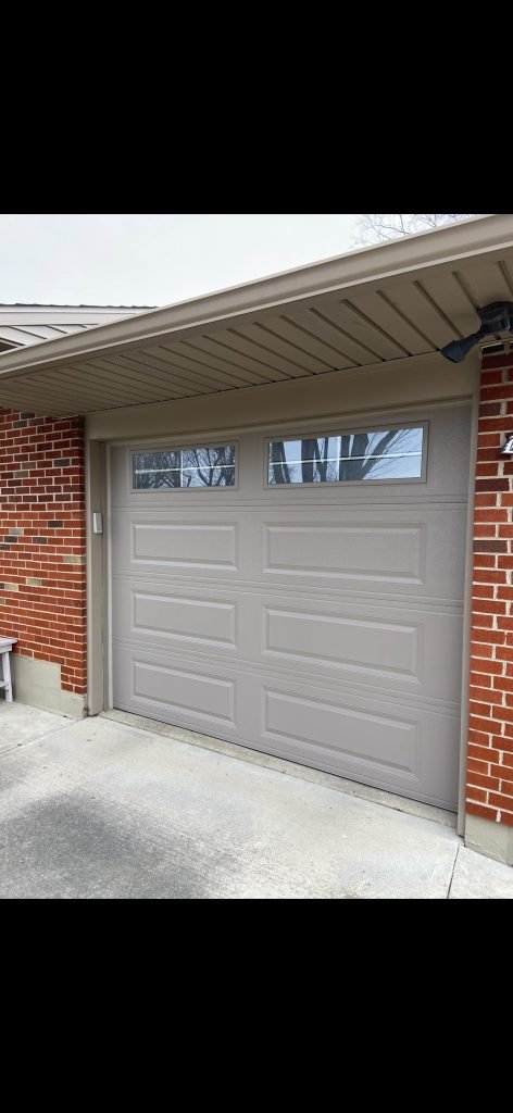 Close-up of a tan garage door with window inserts on a brick home