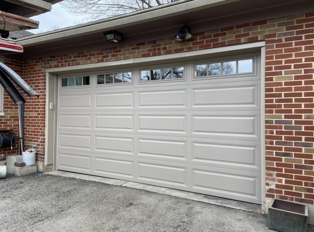 Tan carriage-style garage door with windows on a brick home